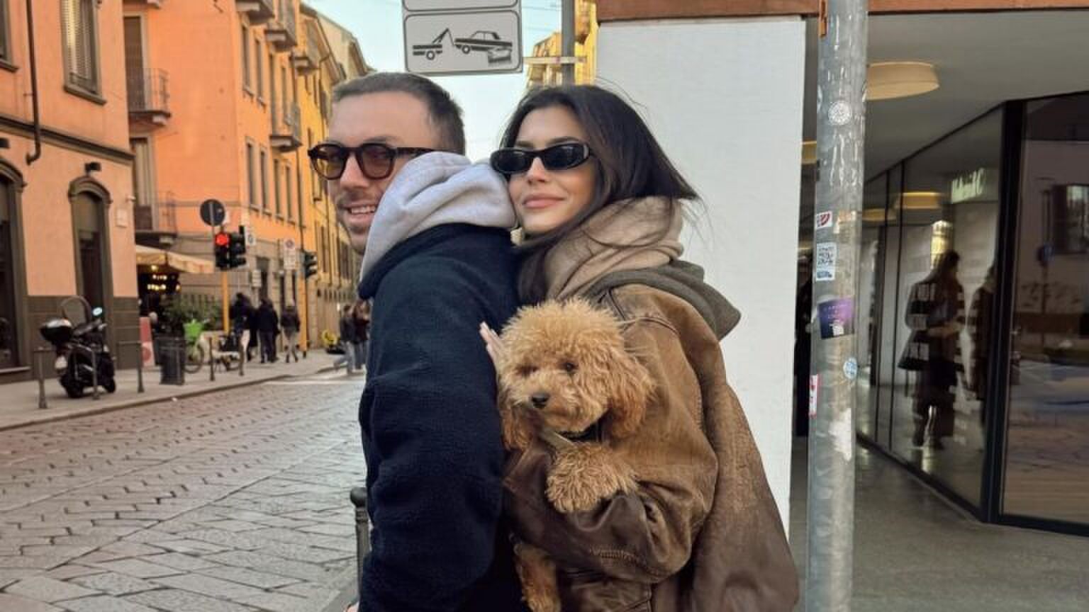 Koppel kijkt lachend over hun schouder. Ze staan op een step. De vrouw heeft een hondje in haar hand.