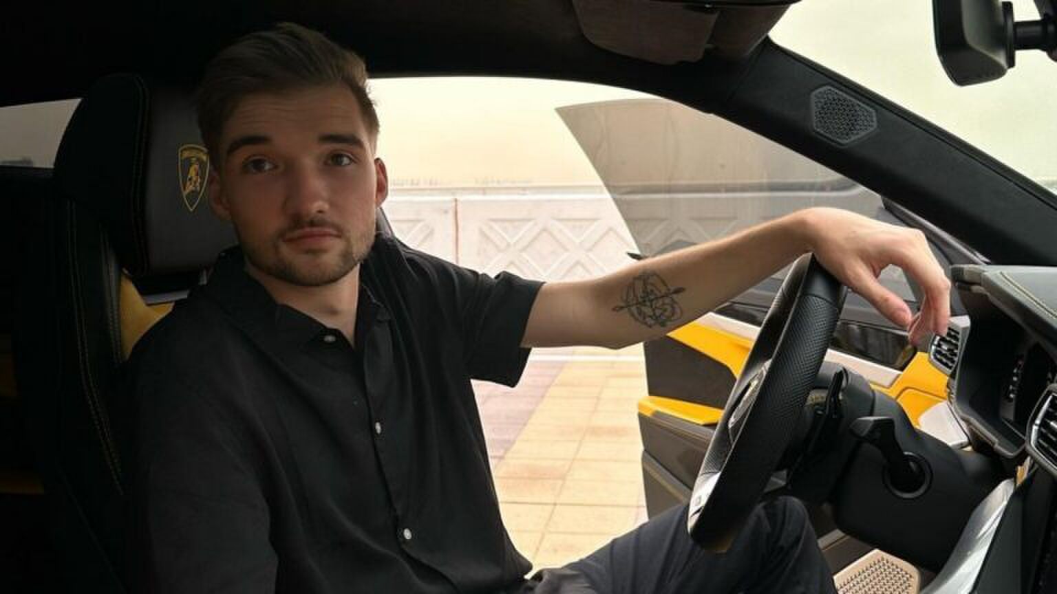 Youtuber Gio Latooy zit in een dure auto. Hij kijkt stoer over zijn schouder.