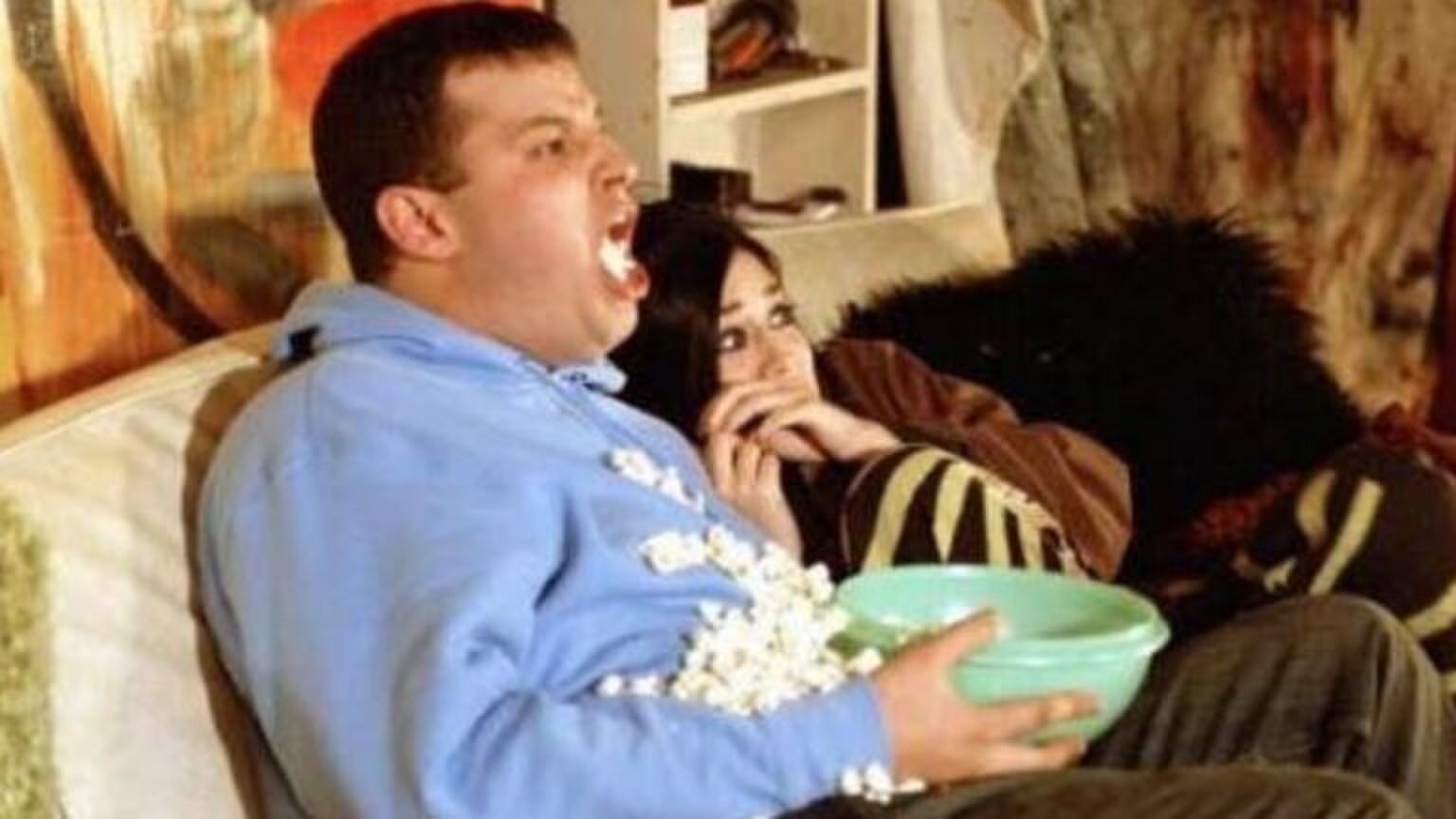 Man en vrouwen schrikken heel erg hard van een horrorfilm. Man spuugt letterlijk zijn popcorn uit. De vrouw duikt ineen.