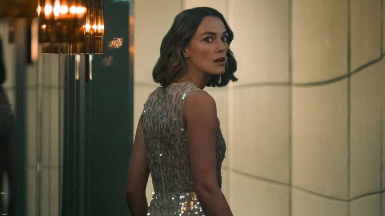 Keira Knightley, die de hoofdrol speelt in de nieuwe film: The Woman in Cabin 10, kijkt angstig over haar schouder. Ze draagt een glitterjurk.