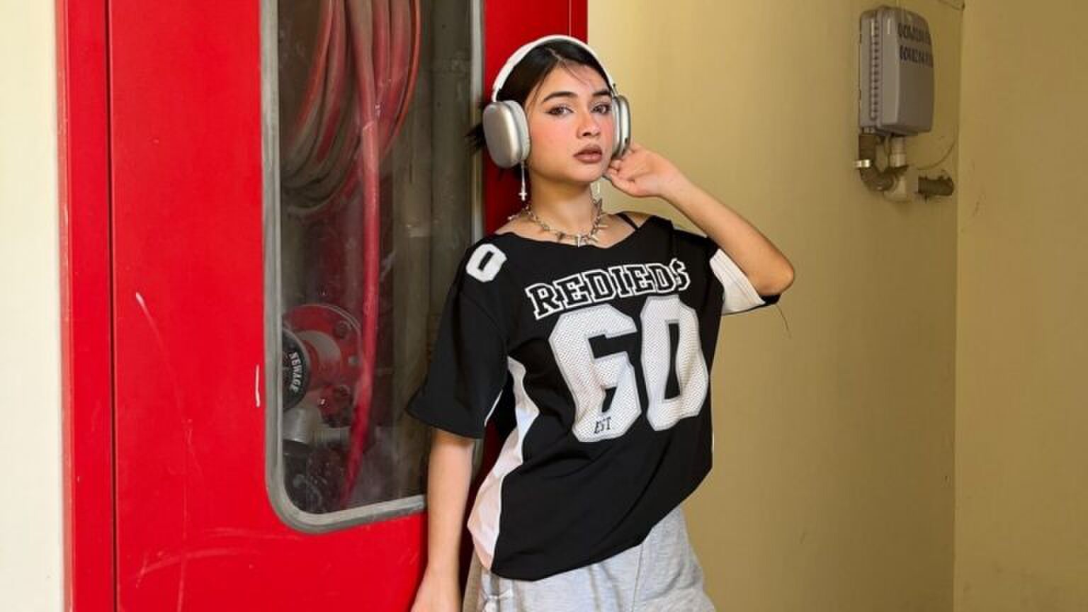 Foto van vrouw die koptelefoon op heeft. Ze leunt tegen een muur aan.