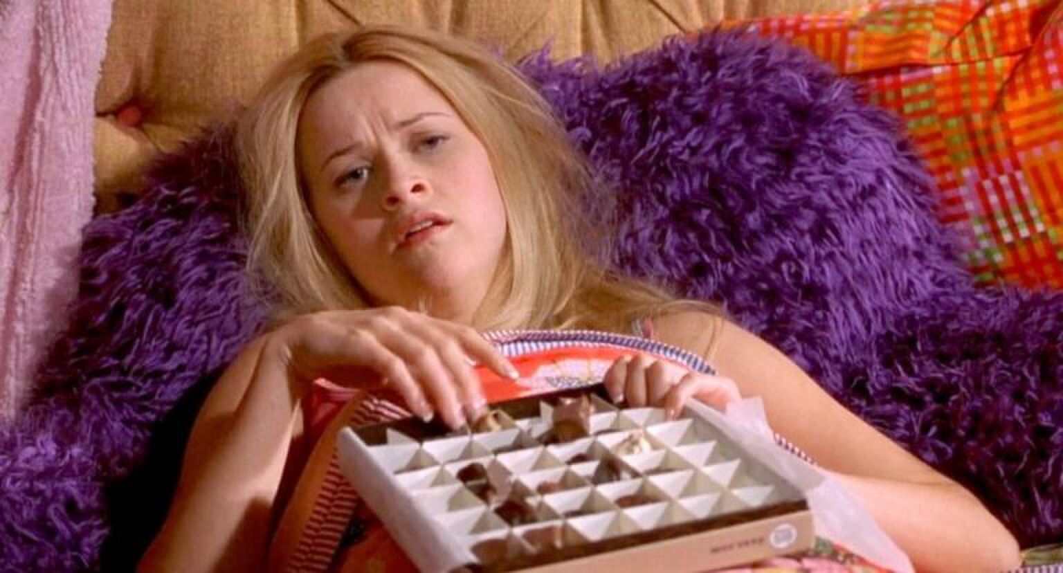 Meisje ligt op bed en eet hele bak chocolaatjes.