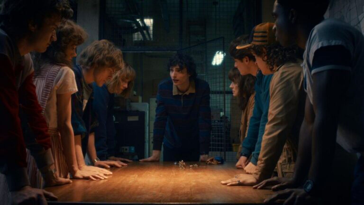 De personages uit Stranger Things staan aan een tafel.