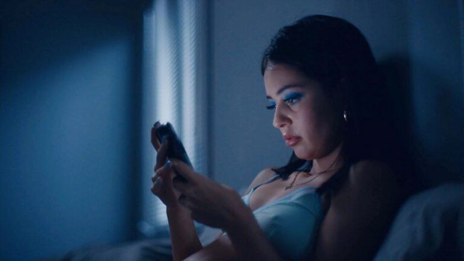 Een vrouw zit in bed in het donker. Ze kijkt naar haar telefoon. Foto uit de HBO-serie: Euphoria.