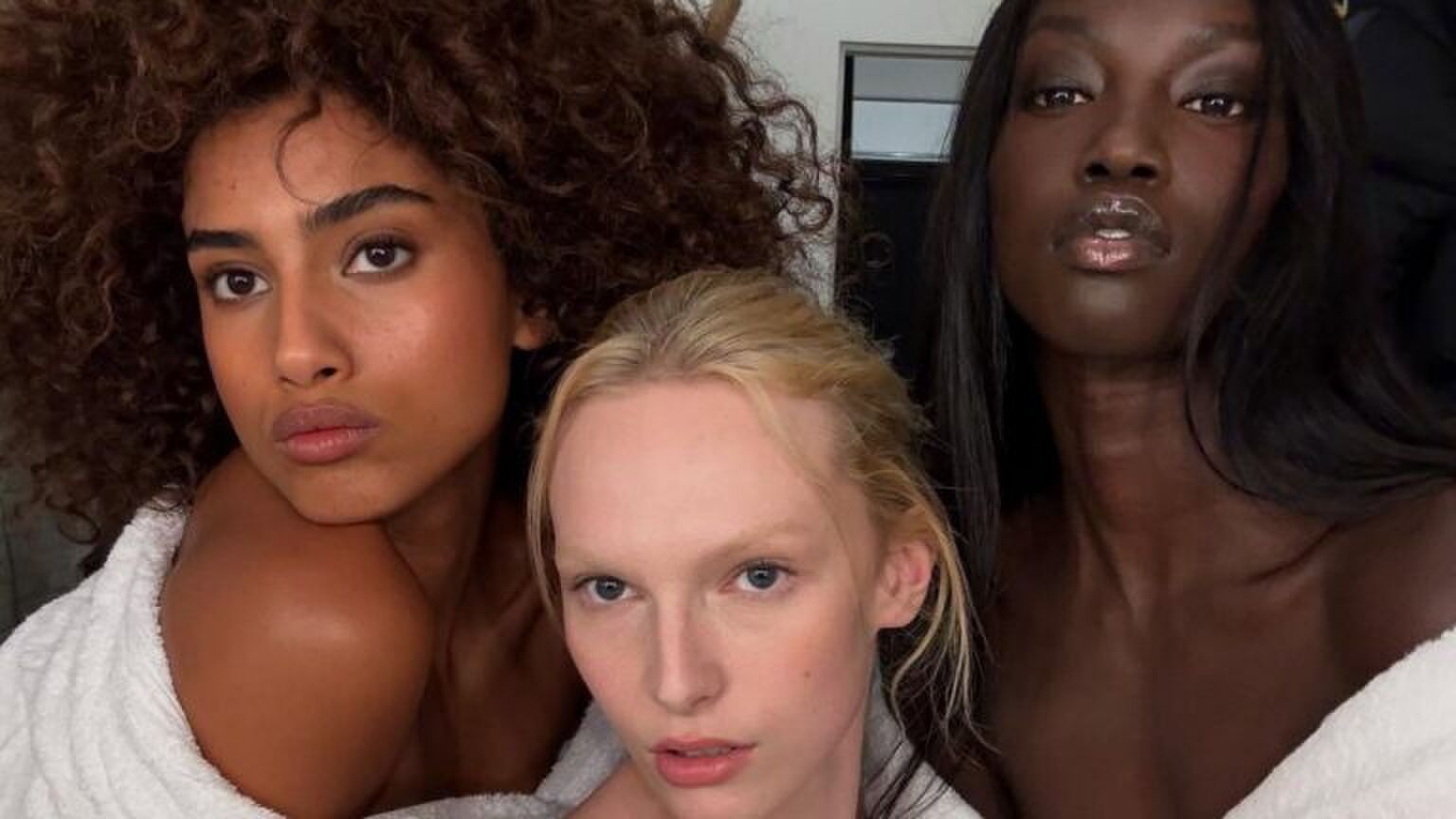 Drie modellen poseren met make-up op in een witte badjas.