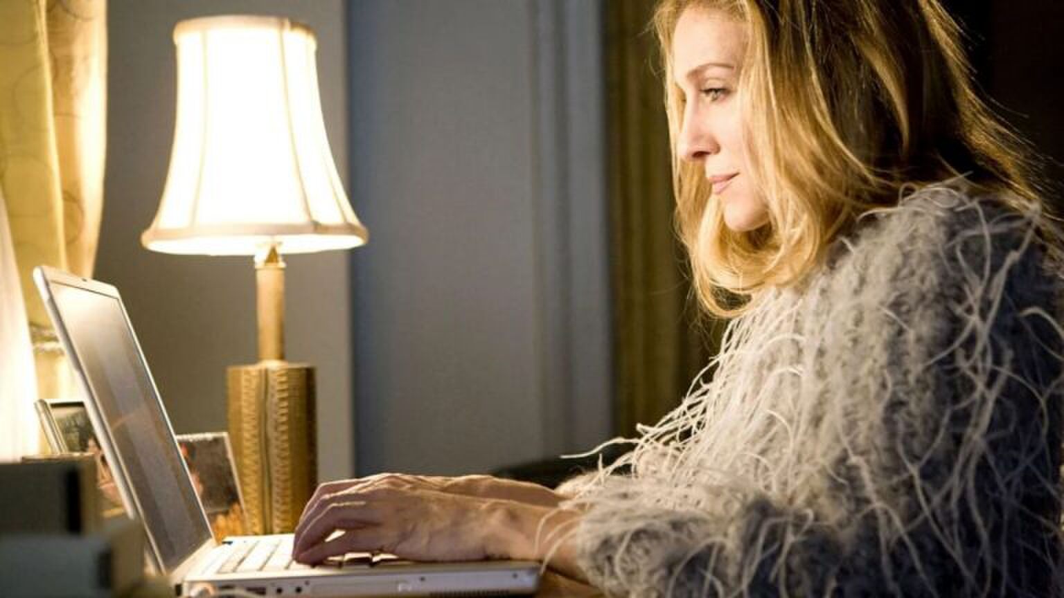Carrie Bradshaw uit Sex And The City zit achter haar laptop.