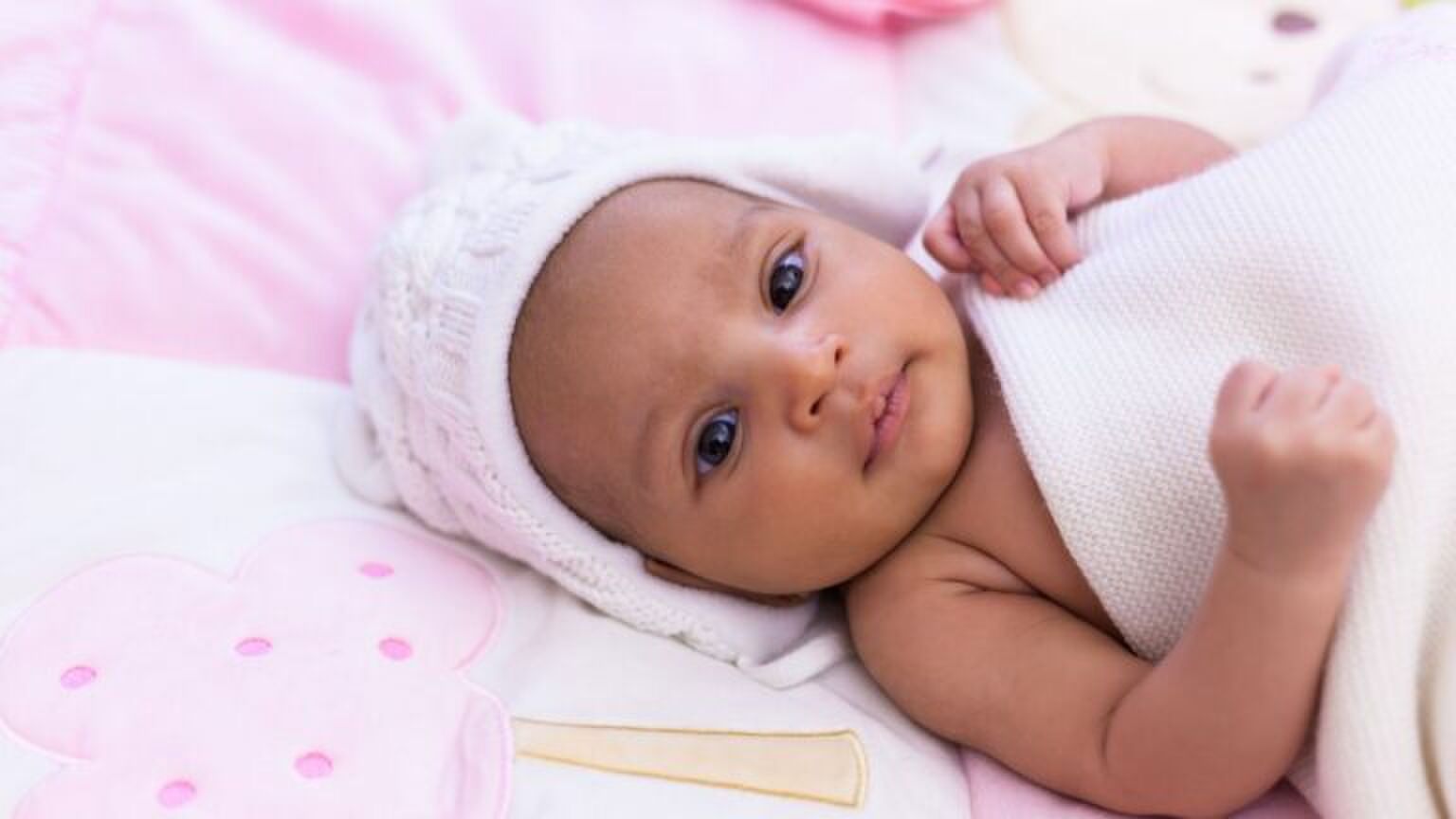 Foto van babymeisje. Ze ligt in een roze bedje.