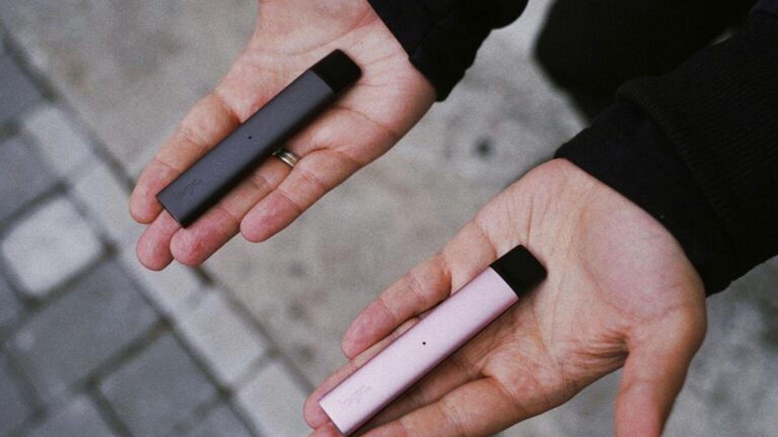 Een man houdt twee vapes vast.