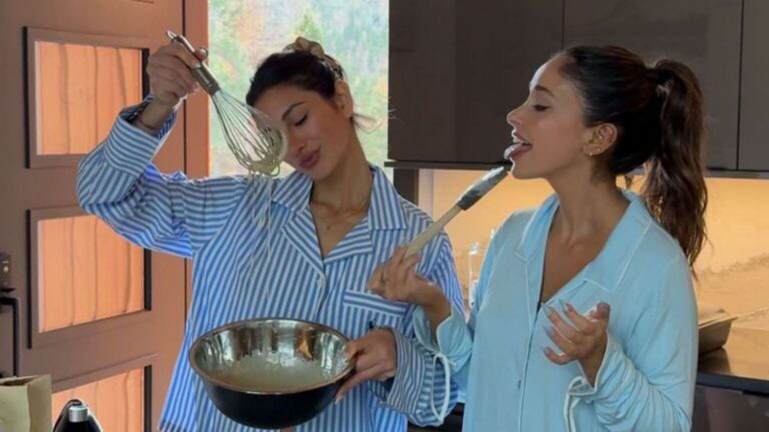 Twee meiden staan in de keuken; ze zijn een taart aan het bakken. De een houdt een garde vast, terwijl de ander aan een spatel likt. Ze zijn erg blij.