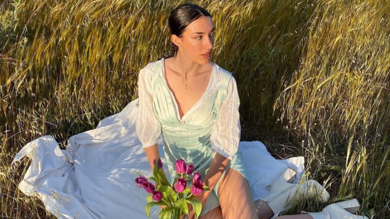 Meisje zit op een kleedje in het gras.