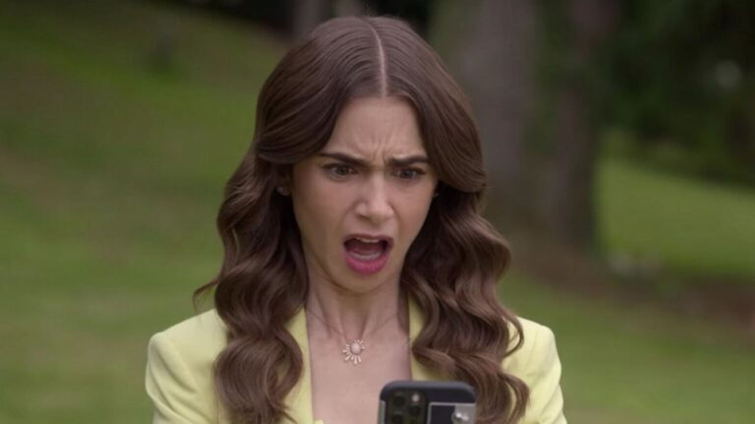 Emily, uit Emily in Paris, kijkt verbaasd naar haar telefoon.