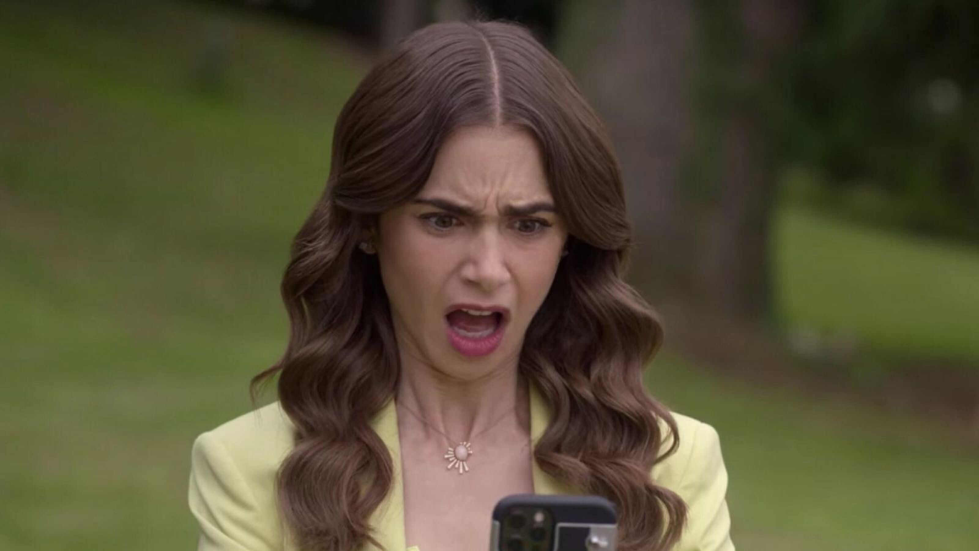 Emily, uit Emily in Paris, kijkt verbaasd naar haar telefoon.