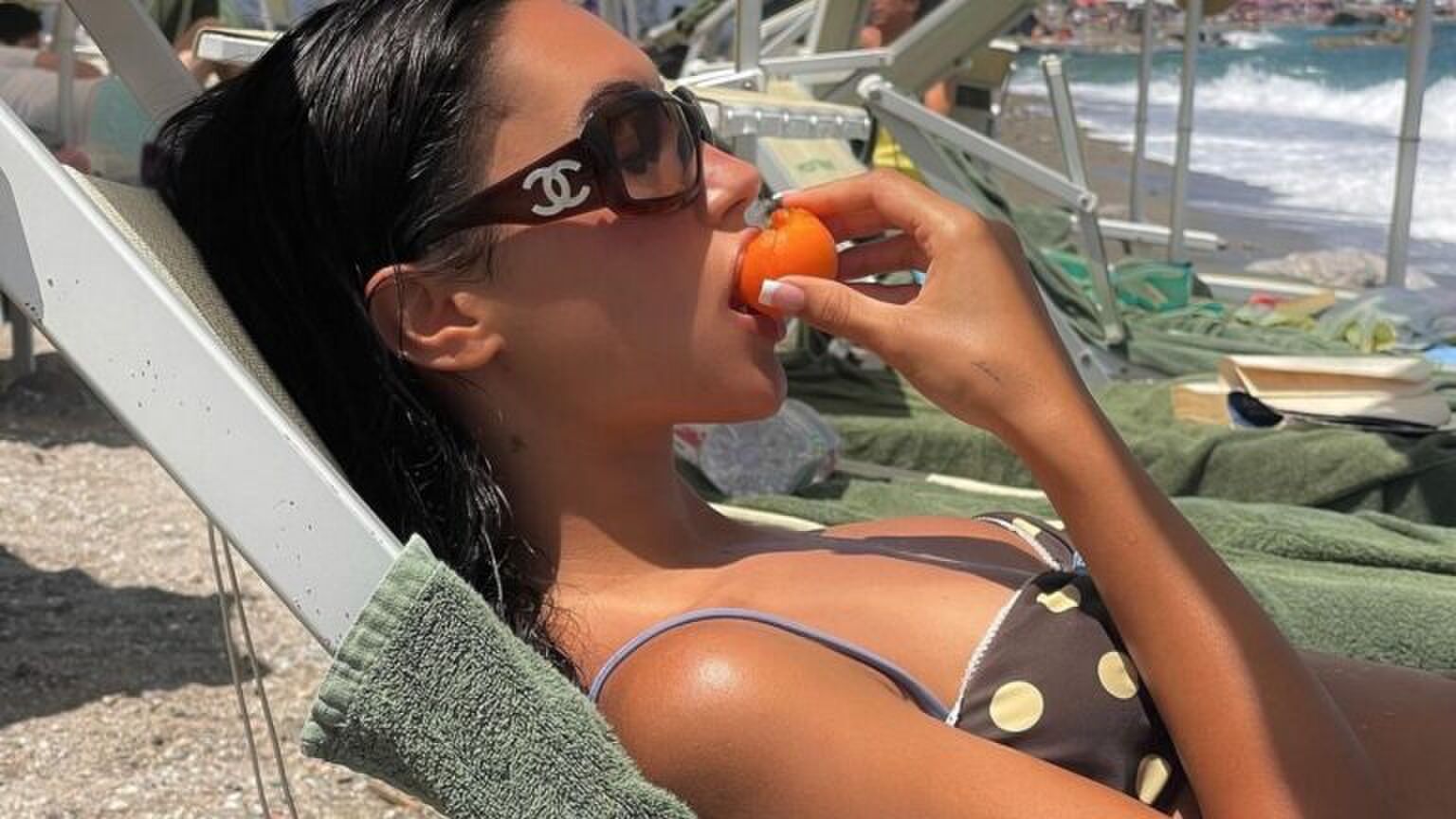 Vrouw ligt op een strandbed. Ze eet een appel.
