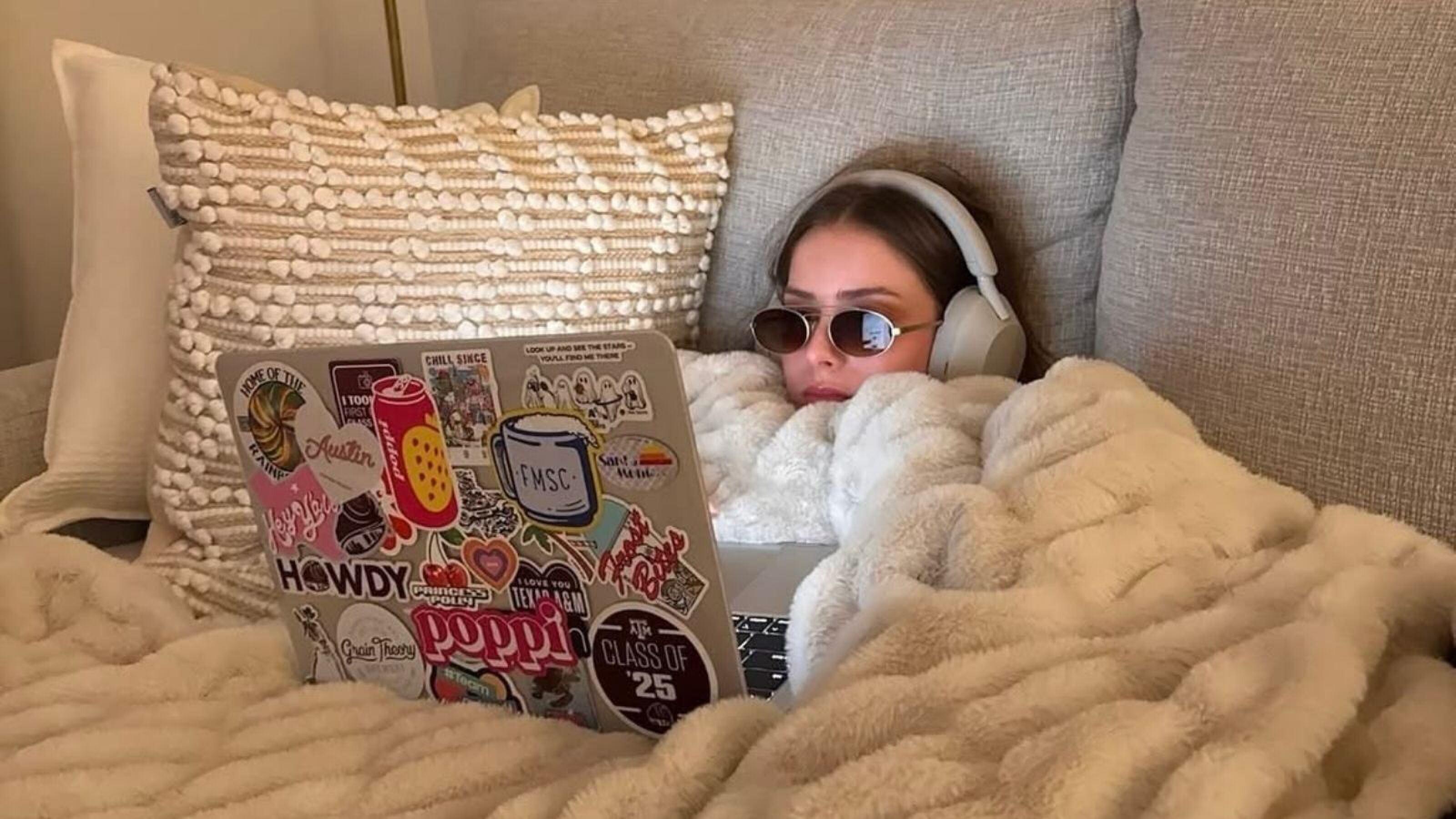 Vrouw in bed met haar laptop, bril en koptelefoon.