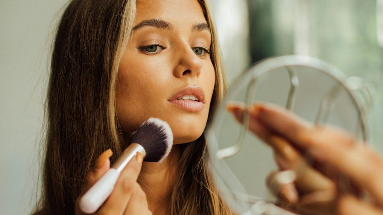 Een vrouw die haar make-up aan het doen is terwijl ze in een spiegel kijkt.