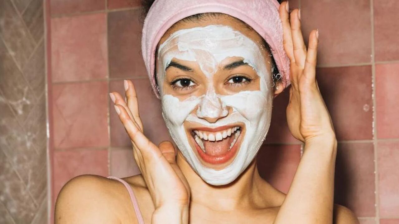 Lachende vrouw met een gezichtsmasker en een handdoek om haar haren.