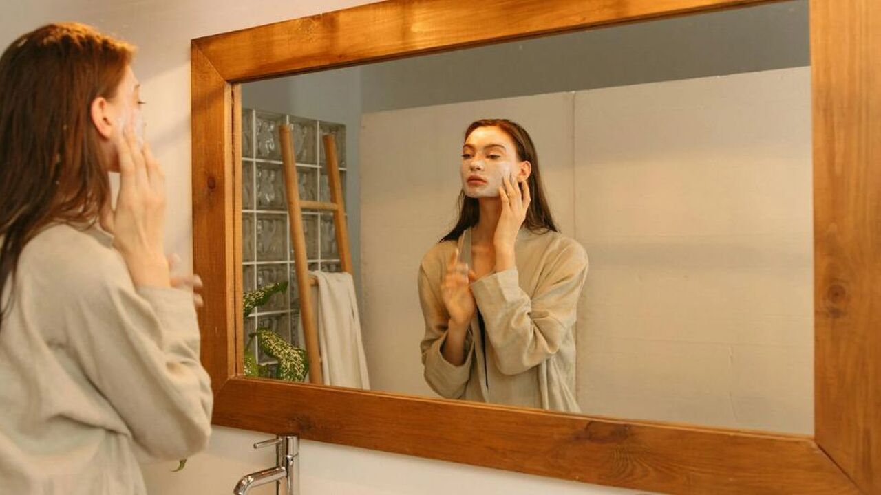 Een vrouw die in een spiegel kijkt terwijl ze een masker aanbrengt op haar gezicht.