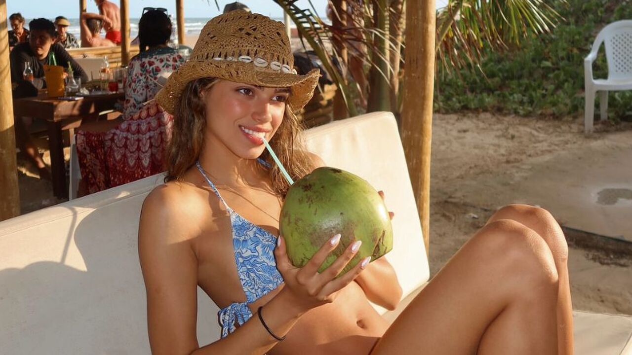 Een vrouw die op een strandbedje uit een kokosnoot drinkt.