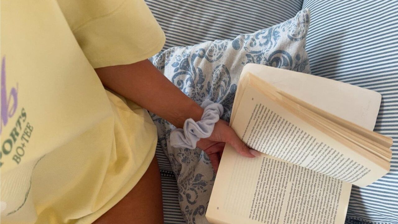 Een gebruinde vrouw zit op haar bed.