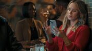 Kristen Bell kijkt vermoeid naar haar telefoon.