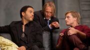 Haymitch, Peeta en Cinna zijn druk in overleg.
