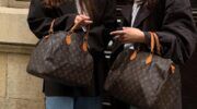 2 meiden die naast elkaar staan met allebei een grote Louis Vuitton tas in hun handen.