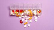 Verschillende rode, gele en witte supplementen in een doorzichtig doosje met een paarse achtergrond.