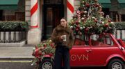 Meisje staat in Londen voor een auto met een kerstboom erop.