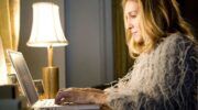Carrie Bradshaw uit Sex And The City zit achter haar laptop.