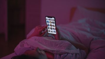Iemand ligt in bed met zijn telefoon.