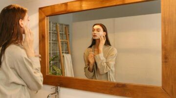 Een vrouw die in een spiegel kijkt terwijl ze een masker aanbrengt op haar gezicht.