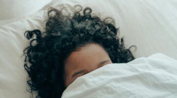 Een kind ligt onder de dekens in bed.