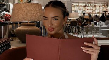 Foto van vrouw die een menukaart vasthoudt in een restaurant. Ze tuit haar lippen.