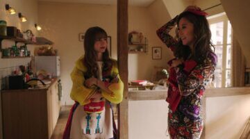 Emily en Mindy uit Emily in Paris staan in hun kleine appartement.