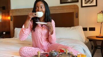 Foto van influencer in hotel. Ze zit op een bed en drinkt een kopje koffie.