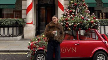 Meisje staat in Londen voor een auto met een kerstboom erop.