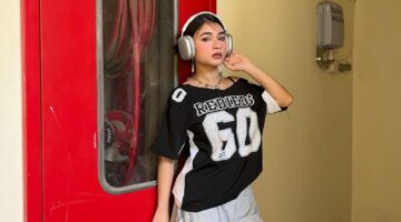 Foto van vrouw die koptelefoon op heeft. Ze leunt tegen een muur aan.