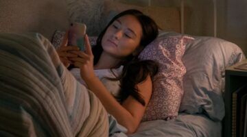 Een jonge vrouw ligt in bed naar haar telefoon te staren.