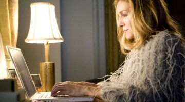 Carrie Bradshaw uit Sex And The City zit achter haar laptop.