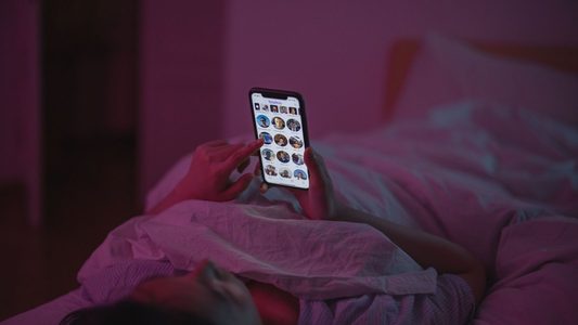 Iemand ligt in bed met zijn telefoon.