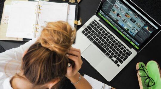 Een vrouw zit achter haar laptop met haar handen in haar haren.
