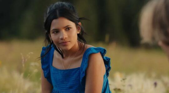 Meisje zit in een weiland in een blauwe jurk.