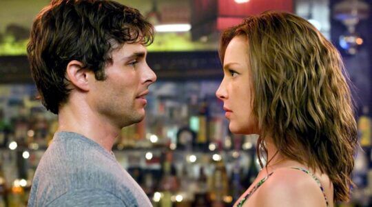 De twee hoofdkarakters van 27 Dresses kijken elkaar intens aan.