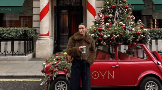 Meisje staat in Londen voor een auto met een kerstboom erop.