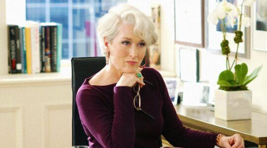 Vrouw zit achter een bureau en kijkt streng.