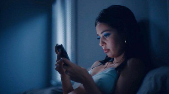 Een vrouw zit in bed in het donker. Ze kijkt naar haar telefoon. Foto uit de HBO-serie: Euphoria.