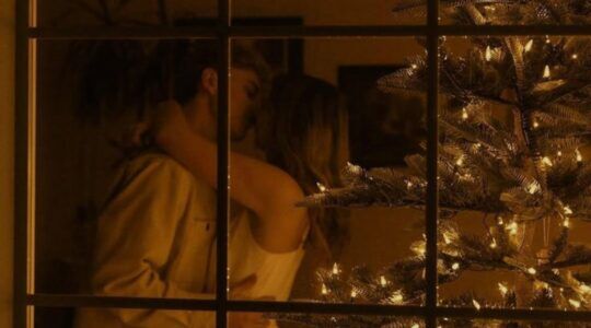 Foto van stelletje dat zoent bij een kerstboom. Ze staan achter een raam.