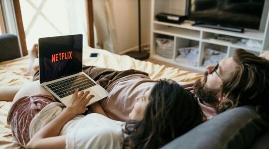 Twee mensen op bed liggen samen en kijken Netflix.