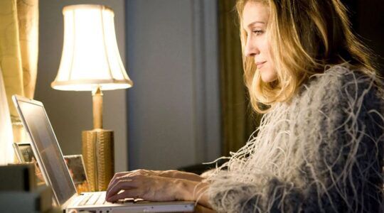 Carrie Bradshaw uit Sex And The City zit achter haar laptop.