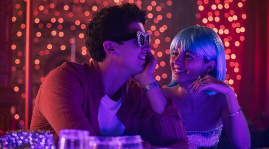 Een jongen met een zonnebril en een meisje met een pruik in een café.